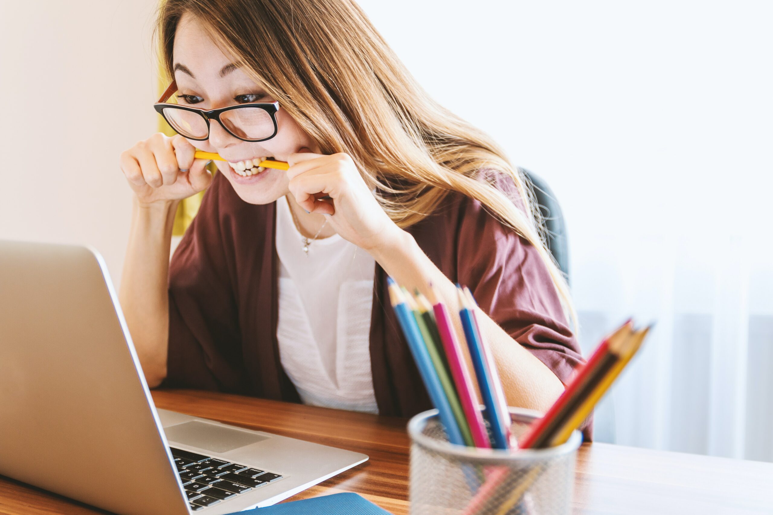 young asian girl chewing a pencil in frustration looking at her laptop screen